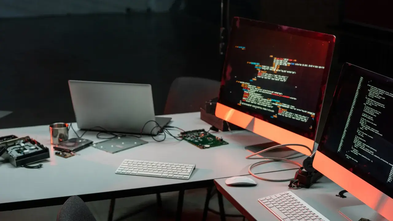 Biurko z komputerami i kodem na ekranach, przygotowane do **mutation testing**. Widać części komputerów i dyski.