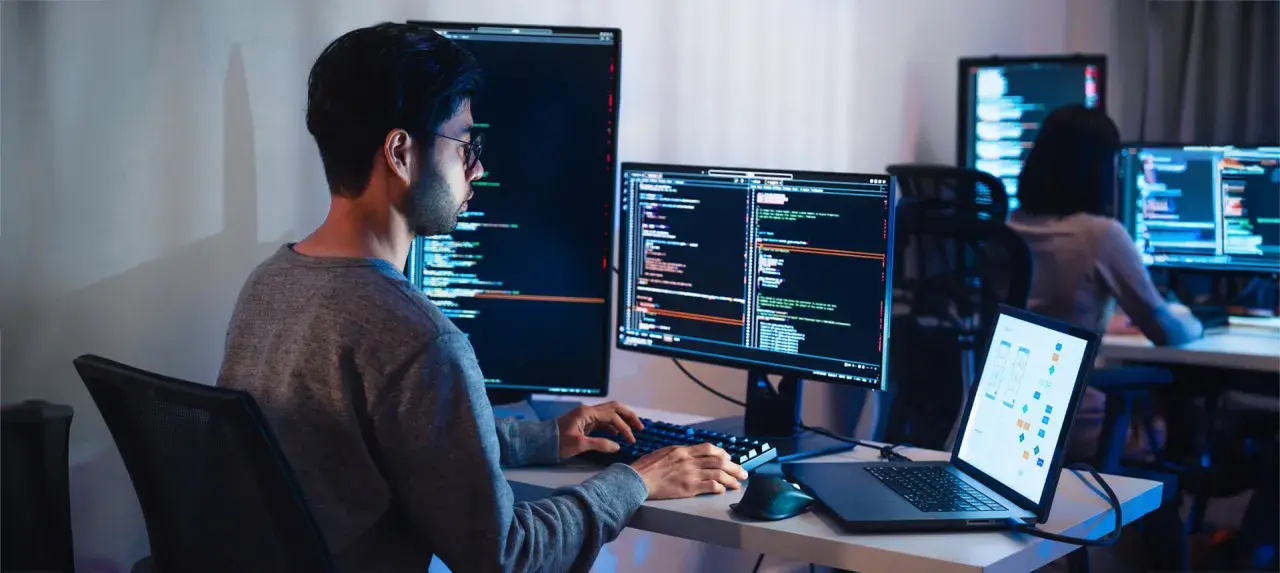 Programista pracuje nad projektem test ai, pisząc kod na wielu monitorach.