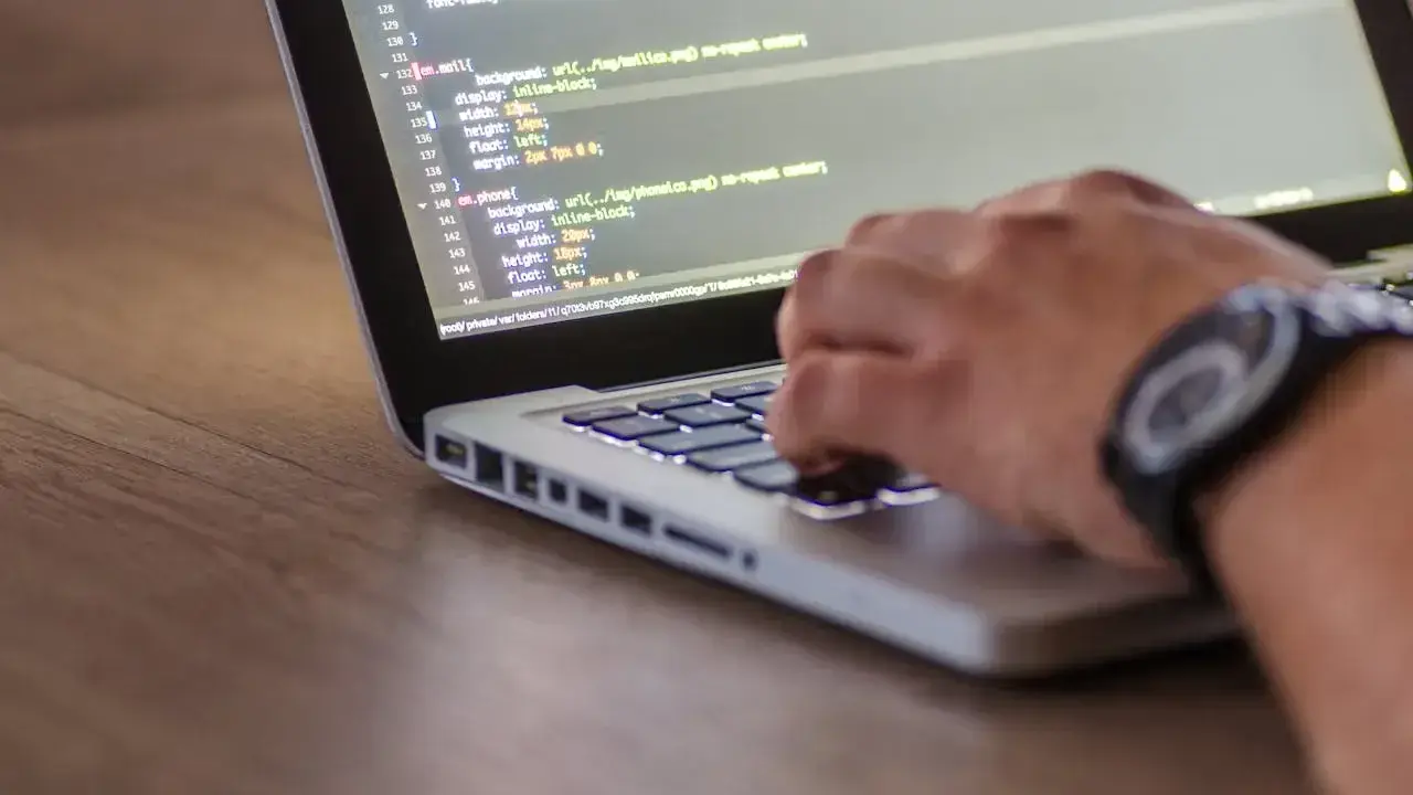 Ręce programisty piszącego kod na laptopie. Tester stron internetowych sprawdza poprawność wyświetlania elementów.