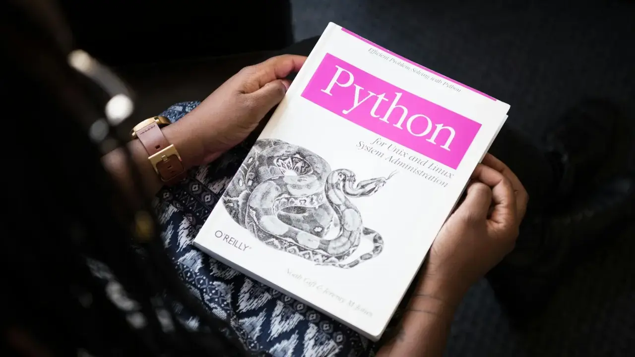Osoba trzyma książkę "Python for Unix and Linux System Administration". To świetna lektura do testowania oprogramowania i nauki Pythona.