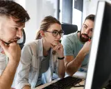 Zespół pracuje nad projektem, analizując kod na ekranie. Skupienie na twarzach sugeruje rozwiązywanie problemów, być może związanych z automatyzacją testów.