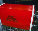 Czerwony, jaskrawy rejestrator lotu, znany jako czarna skrzynka inaczej, z napisem "FLIGHT RECORDER DO NOT OPEN".