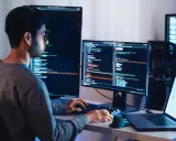 Programista pracuje nad projektem test ai, pisząc kod na wielu monitorach.