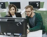 Kobieta i mężczyzna analizują dane na monitorze, dbając o zapewnienie jakości.