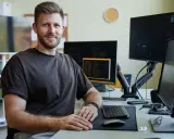 Uśmiechnięty qa engineer siedzi przy biurku z wieloma monitorami, gotowy do testowania oprogramowania.