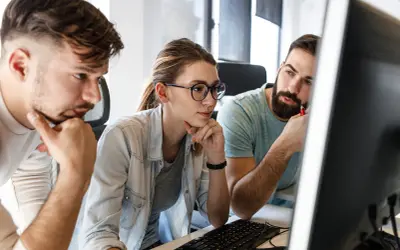 Zespół pracuje nad projektem, analizując kod na ekranie. Skupienie na twarzach sugeruje rozwiązywanie problemów, być może związanych z automatyzacją testów.