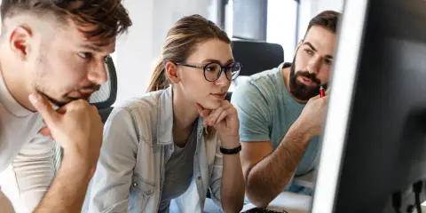 Zespół pracuje nad projektem, analizując kod na ekranie. Skupienie na twarzach sugeruje rozwiązywanie problemów, być może związanych z automatyzacją testów.