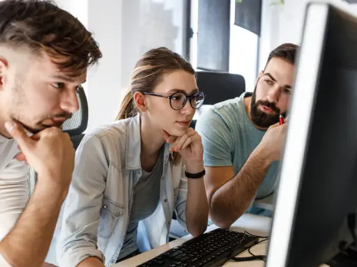 Zespół pracuje nad projektem, analizując kod na ekranie. Skupienie na twarzach sugeruje rozwiązywanie problemów, być może związanych z automatyzacją testów.