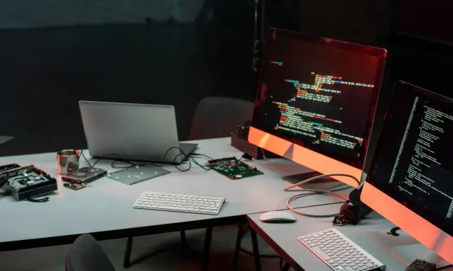 Biurko z komputerami i kodem na ekranach, przygotowane do **mutation testing**. Widać części komputerów i dyski.
