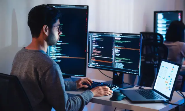 Programista pracuje nad projektem test ai, pisząc kod na wielu monitorach.