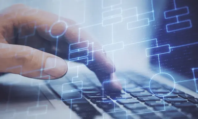 Dłoń na klawiaturze laptopa, nad nią schemat blokowy symbolizujący testy na produkcji.