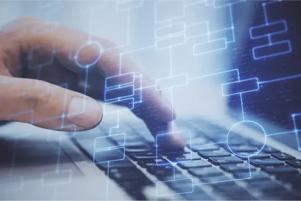 Dłoń na klawiaturze laptopa, nad nią schemat blokowy symbolizujący testy na produkcji.