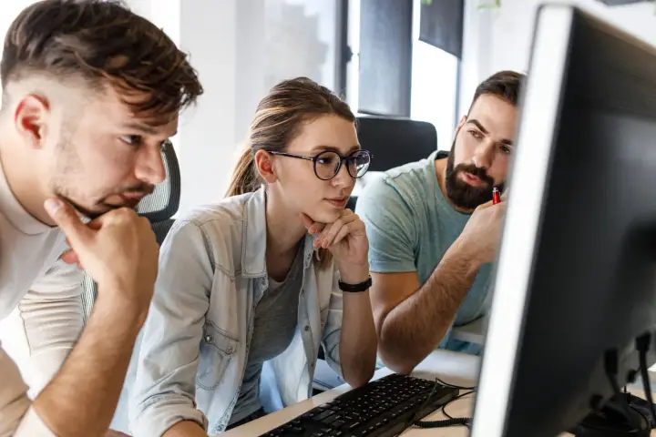 Zespół pracuje nad projektem, analizując kod na ekranie. Skupienie na twarzach sugeruje rozwiązywanie problemów, być może związanych z automatyzacją testów.